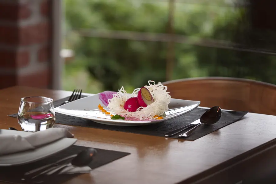 A plated dish with edible flowers on a dark table beside a window onto the garden