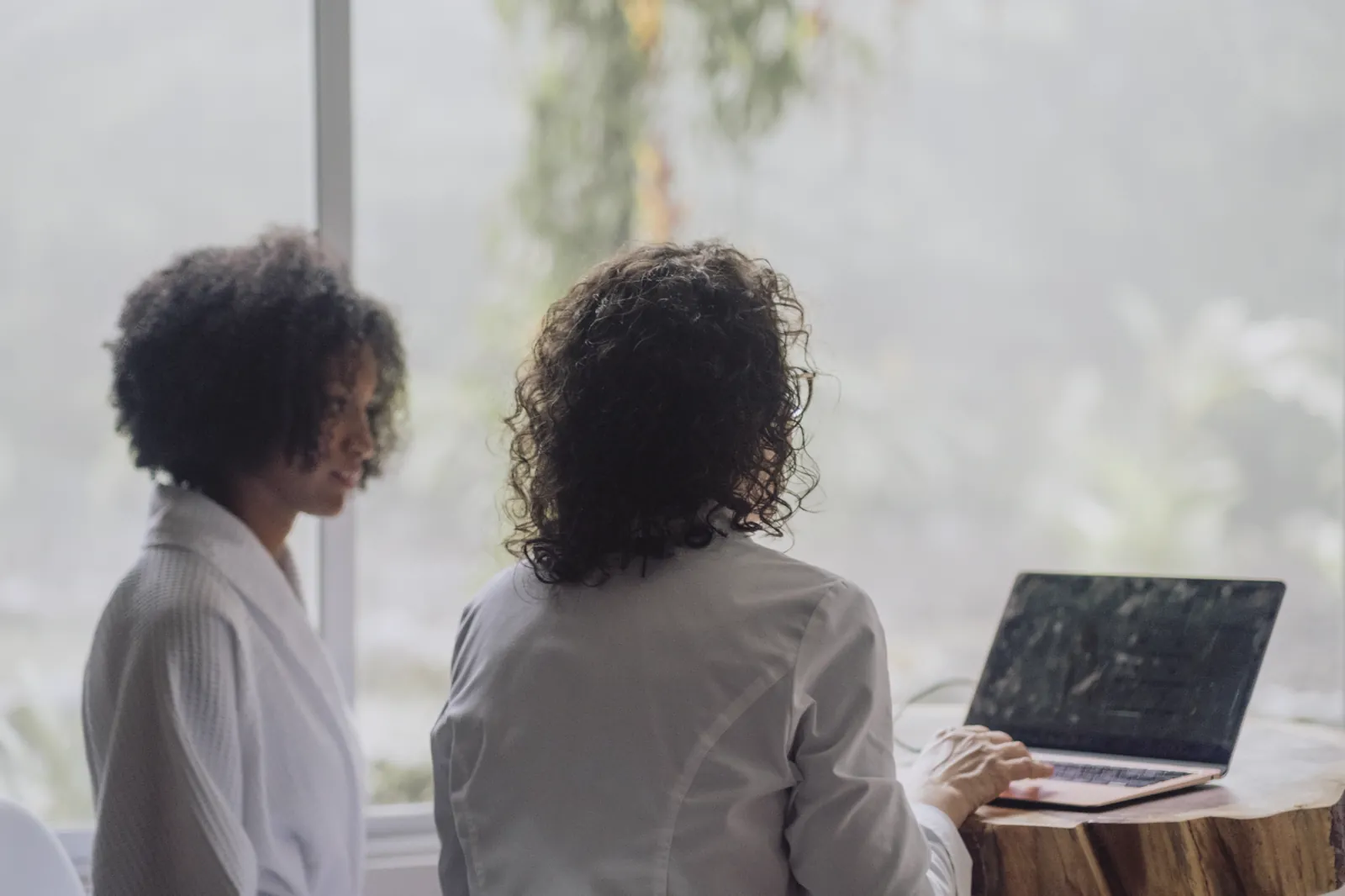 A guest in a robe and the lodge doctor at a wooden table, her readings open between them, the cloud forest in the window behind