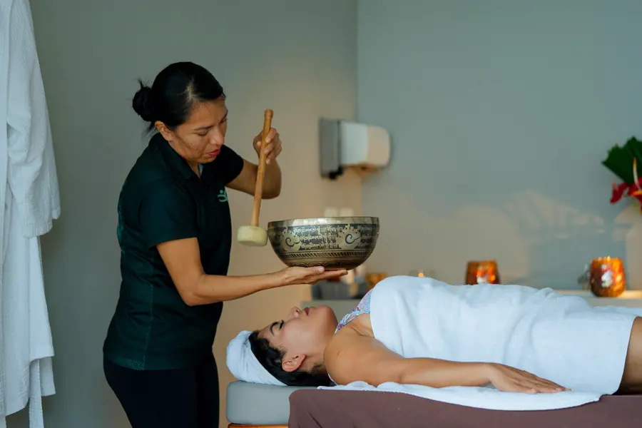 A therapist sounding a metal bowl over a guest resting on a treatment table
